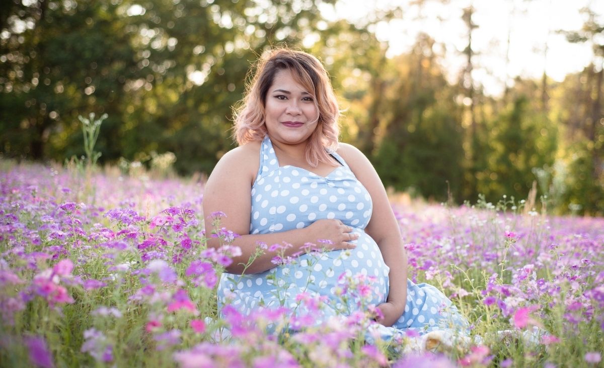 plus size pregnant woman sitting outside in a field of flowers