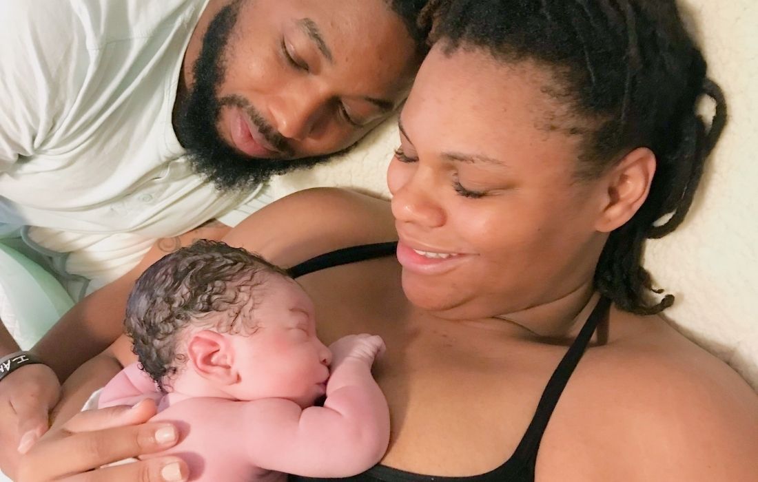 plus size woman, baby, and husband laying in bed following home birth