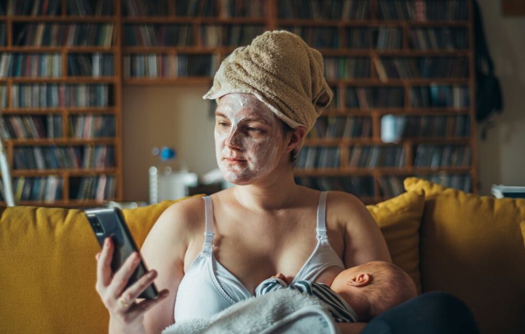 mom during postpartum breastfeeding wearing a face mask and holding phone