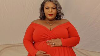 plus size woman wearing a red maternity gown touching her belly
