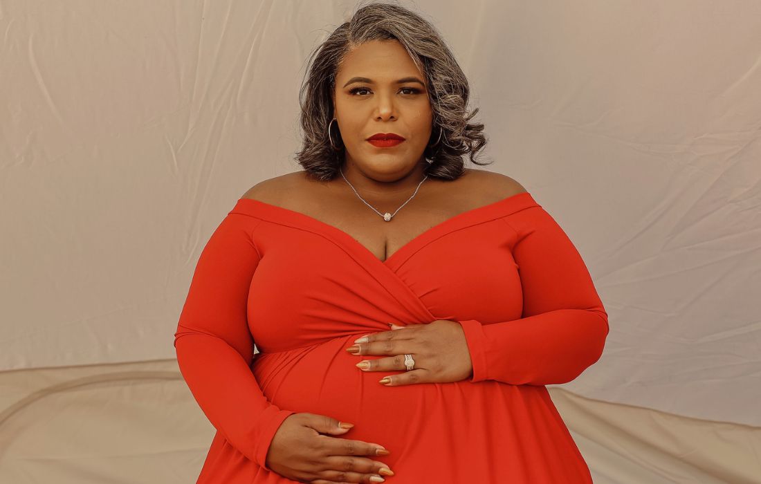plus size woman wearing a red maternity gown touching her belly